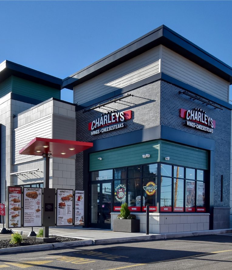 A Charleys Wings & Cheesesteaks restaurant with a drive-thru menu and modern exterior under a clear blue sky.