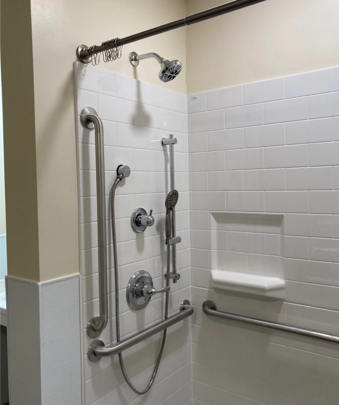ADA compliant shower with grab bars, handheld showerhead, adjustable wall mount, and built-in corner shelf for accessibility.