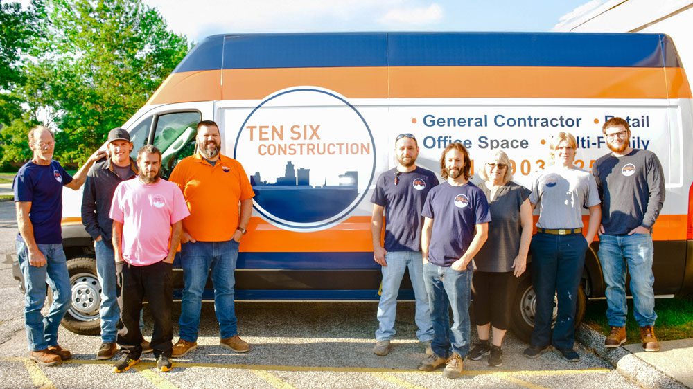Eight people stand in front of a Ten Six Construction van, with company branding and services listed on the side of the vehicle.