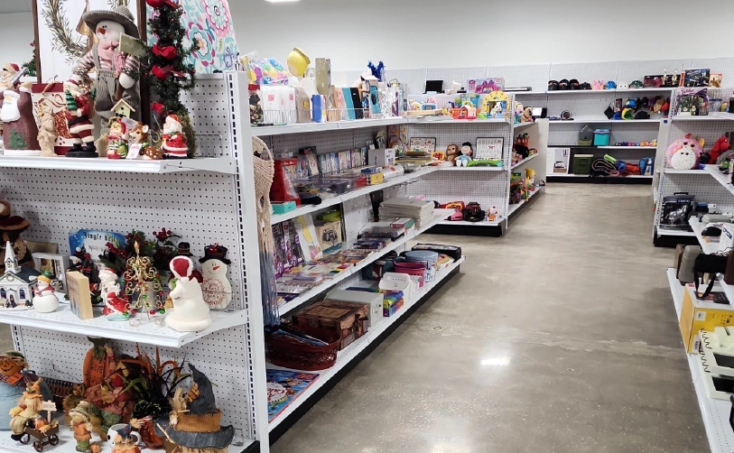 A store aisle with shelves stocked with toys, holiday decorations, stationery, and various household items on a polished concrete floor.
