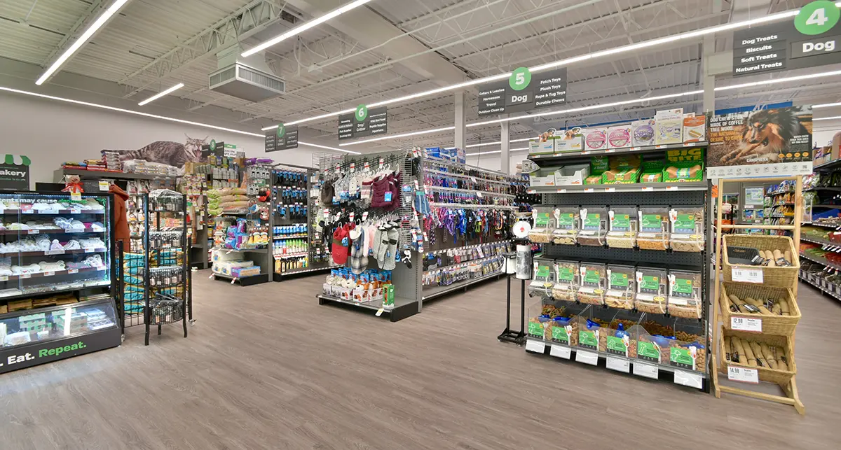 Aisles of a pet supply store displaying dog treats, toys, leashes, and various pet products under bright overhead lighting.
