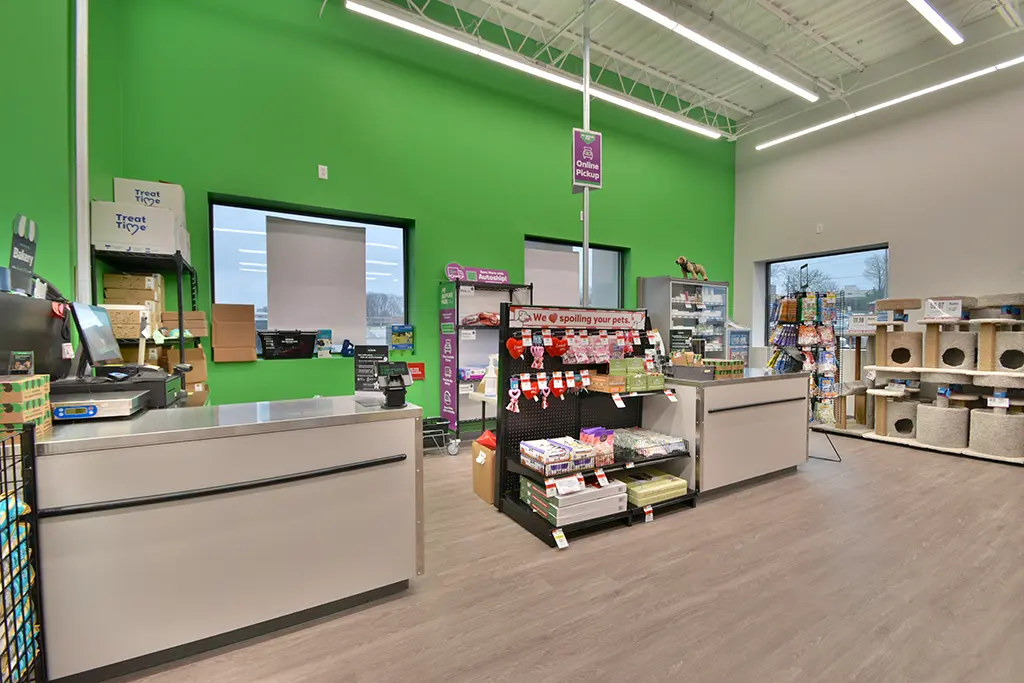 A pet store checkout area with two counters, product displays, green accent wall, and shelves with pet supplies and cat trees.