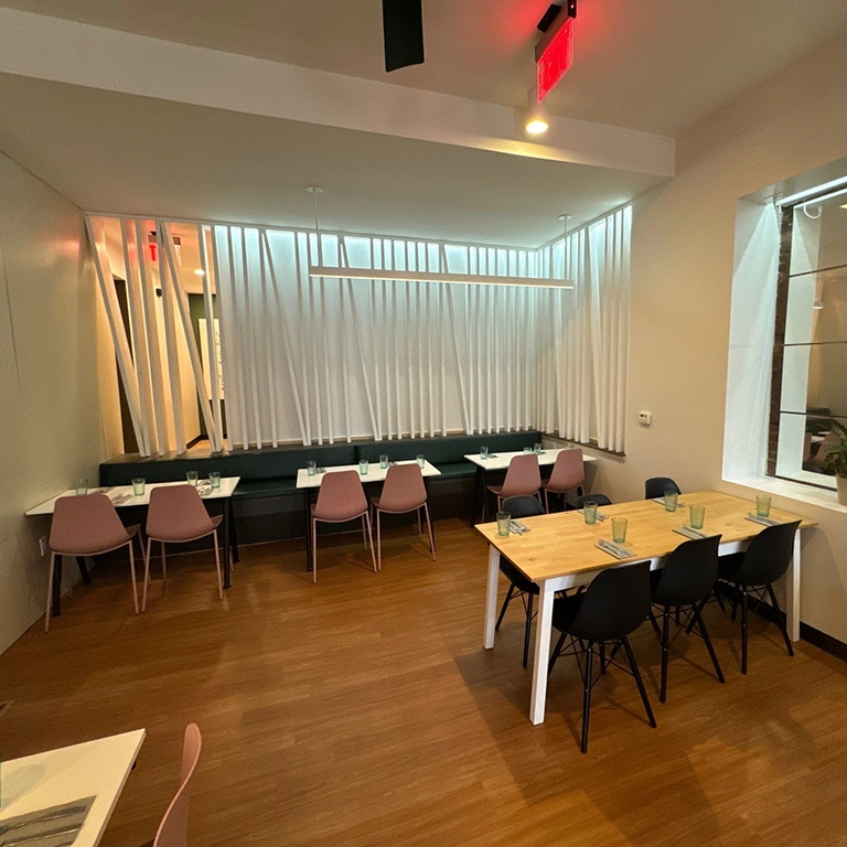 Modern restaurant interior with wooden floor, pink and black chairs, set tables, and a decorative white slatted wall.