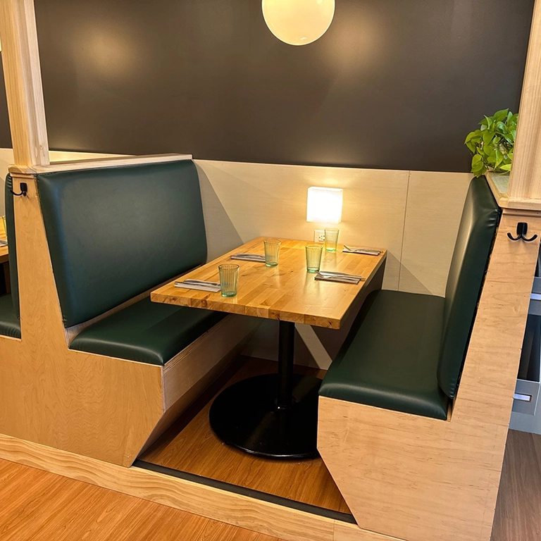 A restaurant booth with green cushioned seats, a wooden table set with glasses and cutlery, and small lamps on the wall.